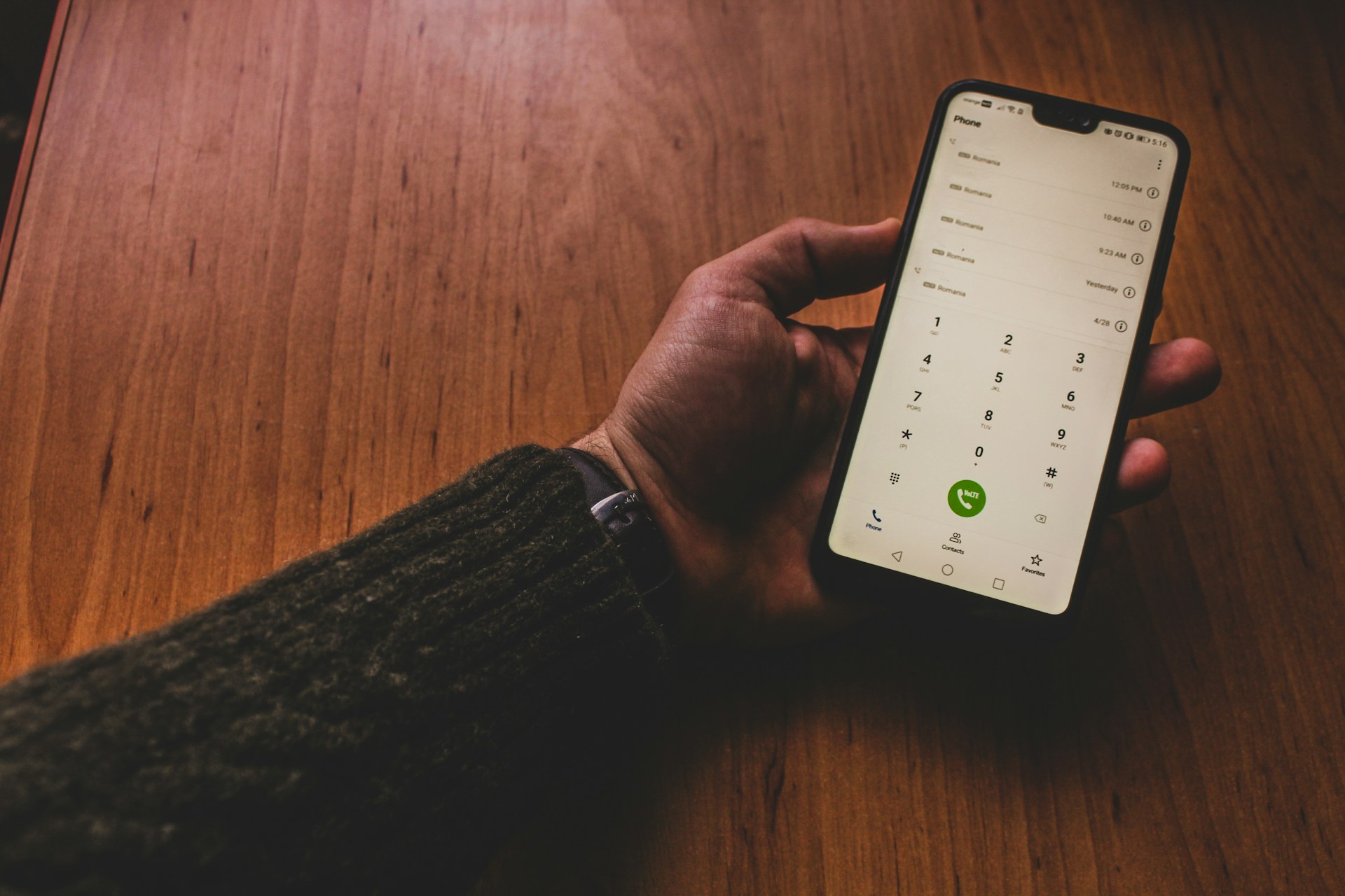 A person holding a smartphone with a green call button, representing mobile communication and home office technology.