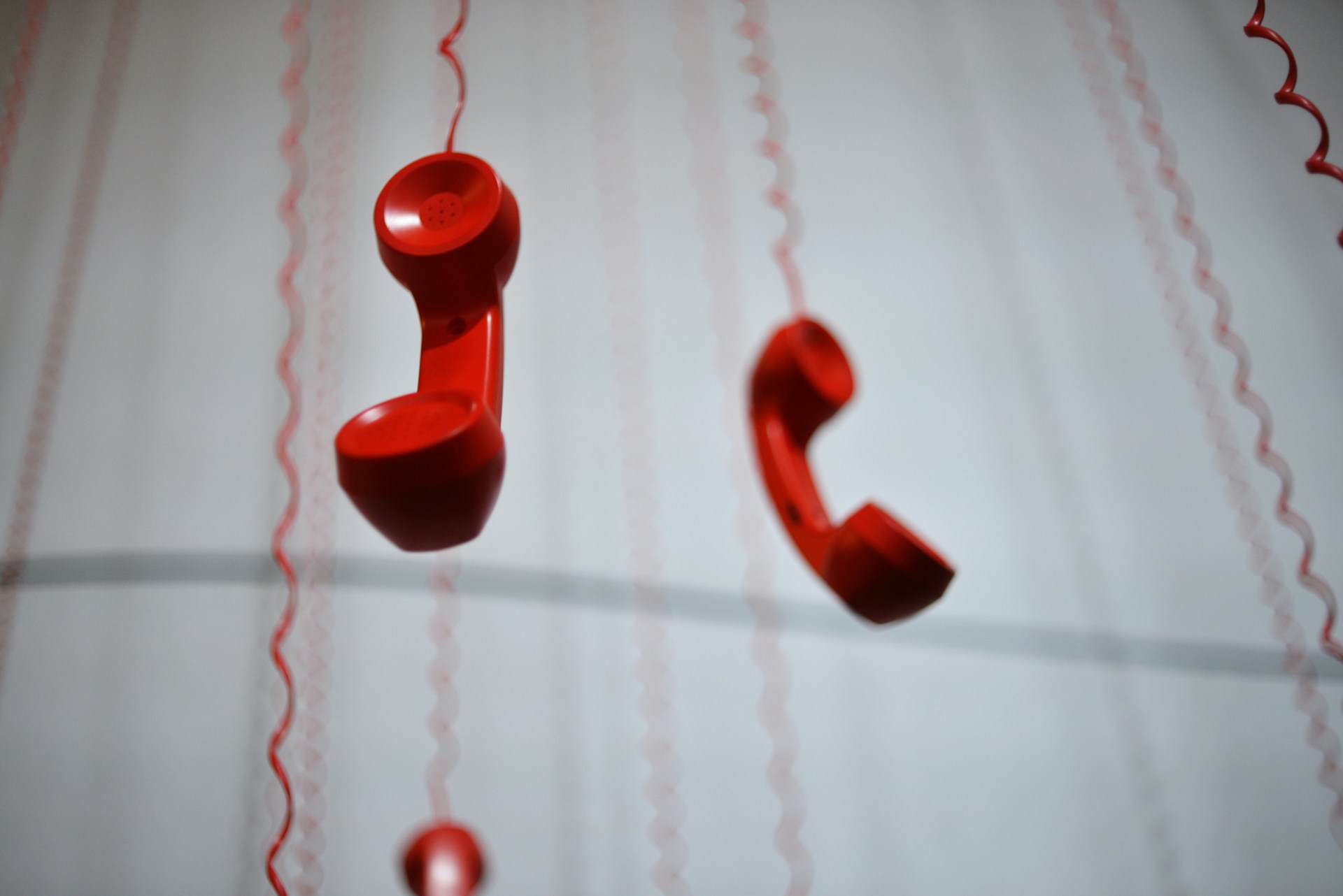 Red vintage phone handsets suspended from above, creating a bold visual symbol of communication.